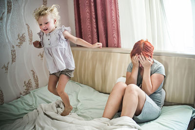 Cheerful daughter near sad mother. happy girl jumps on bed next to outbreaks of bad mood mother. 