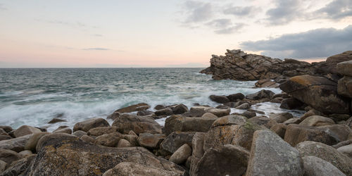 Rocks on shore against sky during sunset