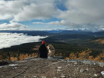 Rear view of woman sitting on mountain against sky