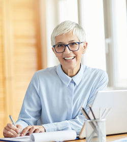 Portrait of smiling senior businesswoman writing on paper