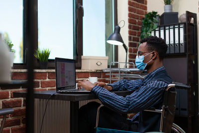 Side view of businessman wearing mask using laptop at office