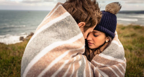 Couple covered with blanket romancing by sea on field