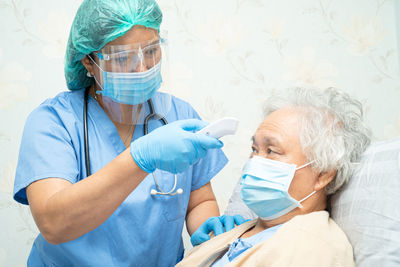 Doctor wearing mask checking temperature of patient at hospital