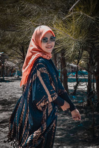 Portrait of young woman standing by tree