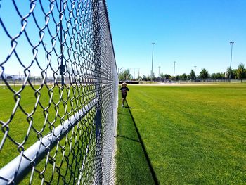 Full length of boy running by fence on baseball field during sunny day