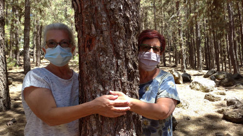 Friends standing by tree trunk in forest