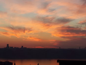 Silhouette city by sea against sky during sunset