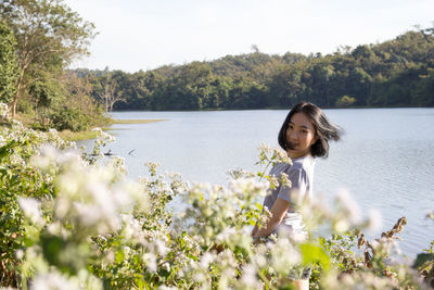 Portrait of young woman standing by plants at lakeshore in forest