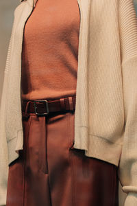 Details of a white knitted sweater and brown trousers with a leather belt. casual women's fashion