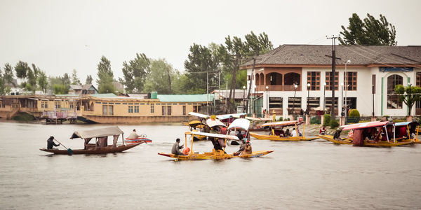 Boats in river by buildings against clear sky. dal lake jammu kashmir, india