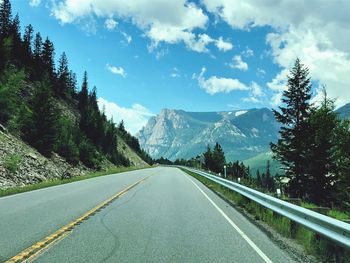 Empty road along trees and mountains against sky