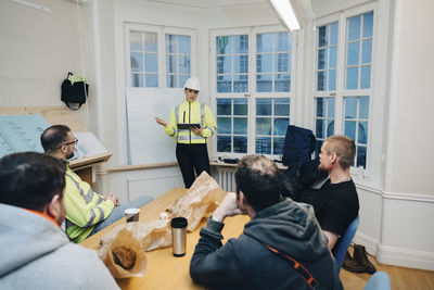 Female building contractor with digital tablet discussing with male colleagues while planning in office