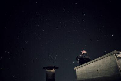 Low angle view of person sitting on retaining wall against star field at night