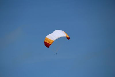 Low angle view of paraglide flying against clear blue sky