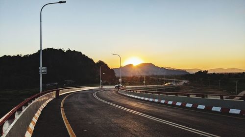 Vehicles on road against sky during sunset
