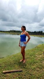 Full length of young woman standing by lake against sky