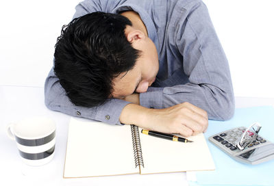 Portrait of frustrated man putting head down on desk against white background