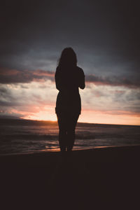 Silhouette woman standing on beach against sky during sunset