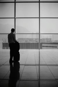 Rear view of silhouette man standing by window