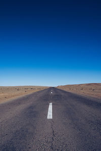 Road passing through landscape against clear blue sky