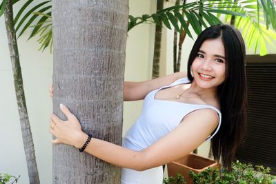 Portrait of smiling young woman standing by tree trunk