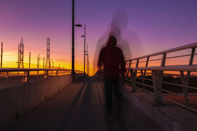 Blurred motion of man walking on bridge against sky during sunset