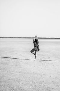 Rear view of woman doing yoga at beach against clear sky