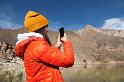 Rear view of person photographing by lake against sky during winter