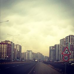 Road passing through city against cloudy sky