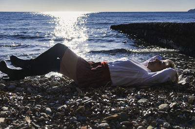 Woman lying on shore at beach against sky