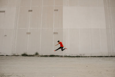 Side view of man running against red wall
