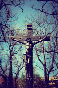 Low angle view of cross statue against bare trees