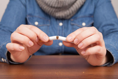 Midsection of woman breaking cigarette at table