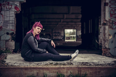 Portrait of young woman sitting by abandoned building
