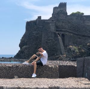 Full length of man sitting on rock against sky