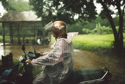 Woman sitting on motorcycle against trees