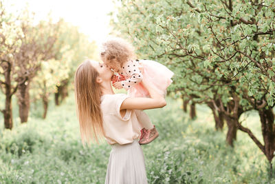Mother carrying daughter and kissing her standing on grass