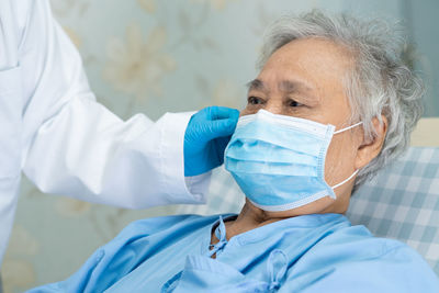 Midsection of doctor wearing mask to senior woman in hospital