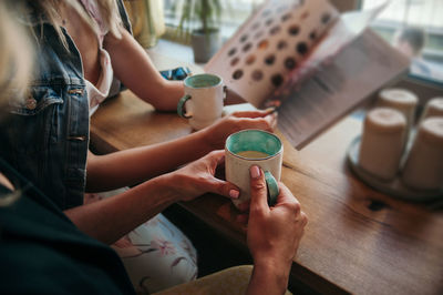 Women's hands with pastel manicure hold ceramic mugs white on the outside mint inside with cafe