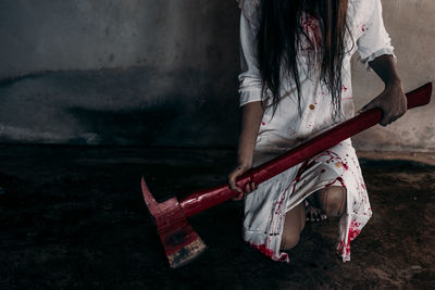Midsection of evil woman holding knife covered with blood against wall