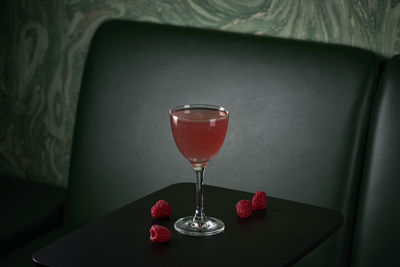 Pink cocktail with raspberries in front of green sofa