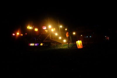 Illuminated street lights on field against sky at night