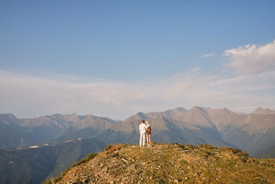 Rear view of couple standing on mountain peak against sky