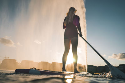 Rear view of woman standing by boat against sky during sunset