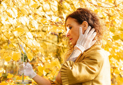 Close-up of mature woman holding hand mirror standing by autumn tree