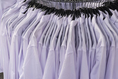 High angle view of white shirts hanging from coathangers on rack at clothing store