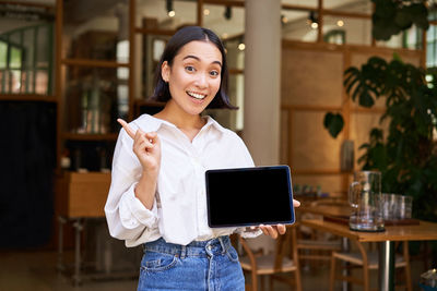 Portrait of young woman using mobile phone while standing in cafe