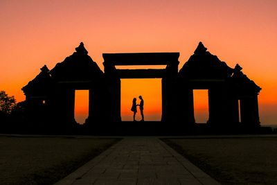 Silhouette man and woman standing at ratu boko against clear sky during sunset