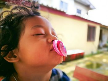 Close-up of boy with pacifier in mouth against house