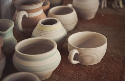 Many clay pot is on the table in pottery. bright pottery. many white, not painted clay pottery 